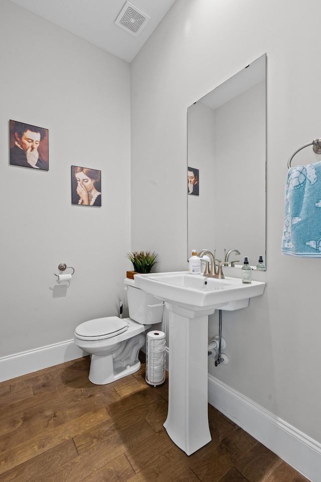 half bathroom featuring visible vents, baseboards, wood finished floors, and toilet