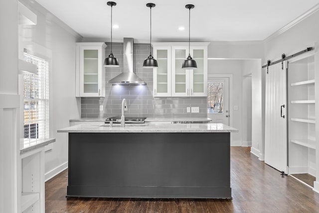 kitchen with wall chimney range hood, white cabinets, ornamental molding, and a barn door