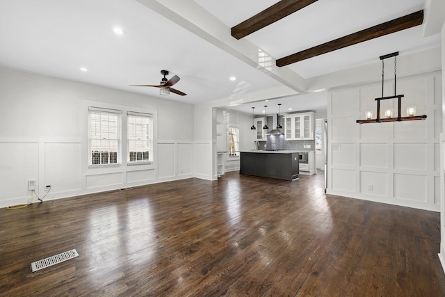 unfurnished living room featuring visible vents, dark wood-type flooring, ceiling fan with notable chandelier, and a decorative wall
