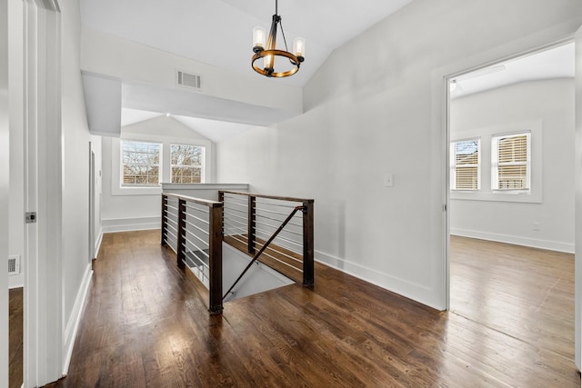 corridor with a chandelier, an upstairs landing, wood finished floors, vaulted ceiling, and visible vents