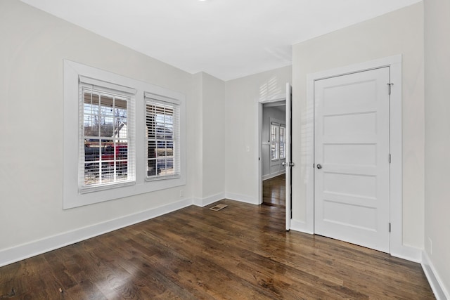 unfurnished room with baseboards, dark wood finished floors, and visible vents