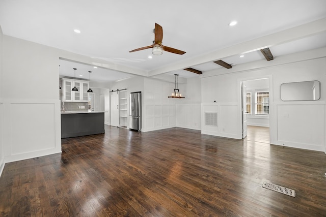 unfurnished living room with visible vents, a barn door, ceiling fan, and a decorative wall