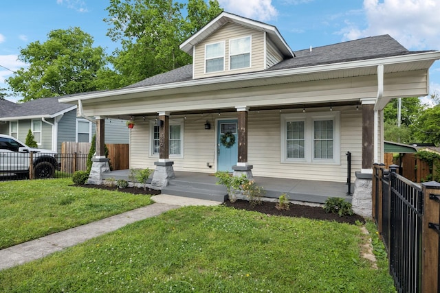 bungalow-style house with covered porch, fence, a shingled roof, and a front yard