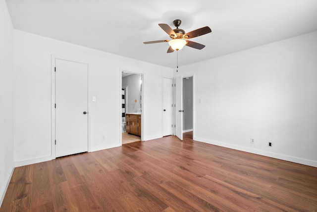 unfurnished bedroom featuring a ceiling fan, baseboards, wood finished floors, and ensuite bathroom