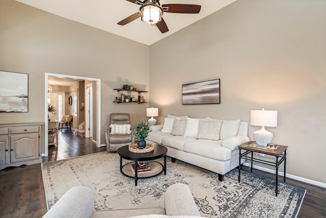 living area featuring baseboards, a ceiling fan, dark wood-style flooring, and high vaulted ceiling