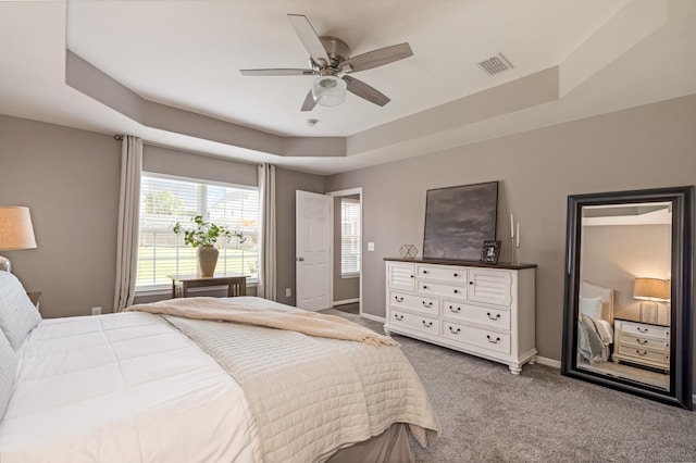 bedroom featuring carpet floors, visible vents, baseboards, a tray ceiling, and a ceiling fan