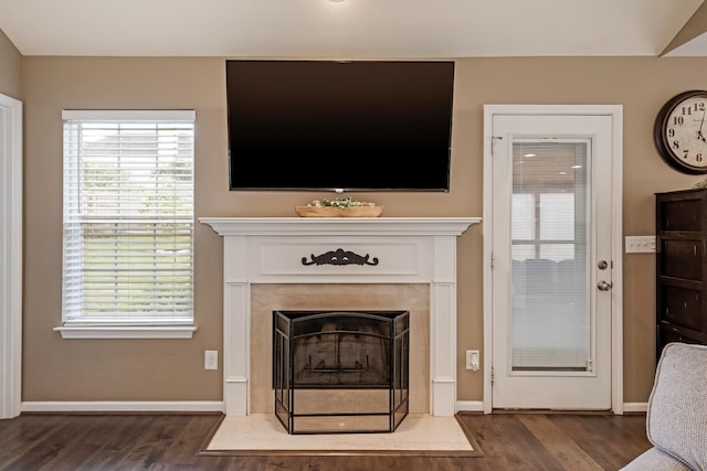living room featuring baseboards, a fireplace with flush hearth, plenty of natural light, and dark wood-type flooring