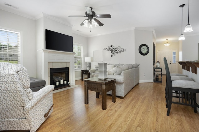 living room featuring ceiling fan, a fireplace, light wood-style flooring, baseboards, and visible vents