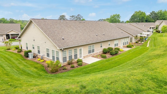 back of house with a lawn, a shingled roof, a patio area, and central AC