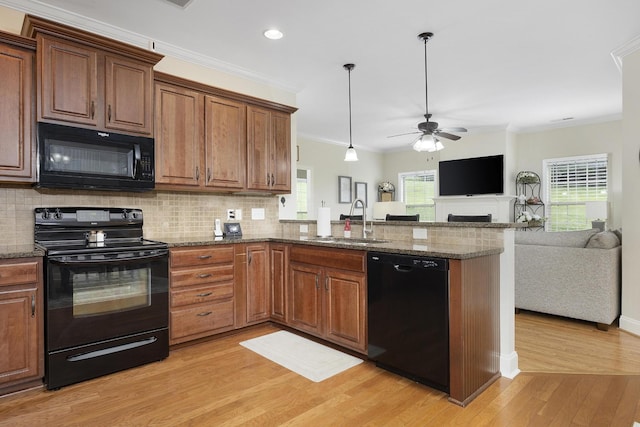 kitchen with a sink, light wood finished floors, a peninsula, open floor plan, and black appliances