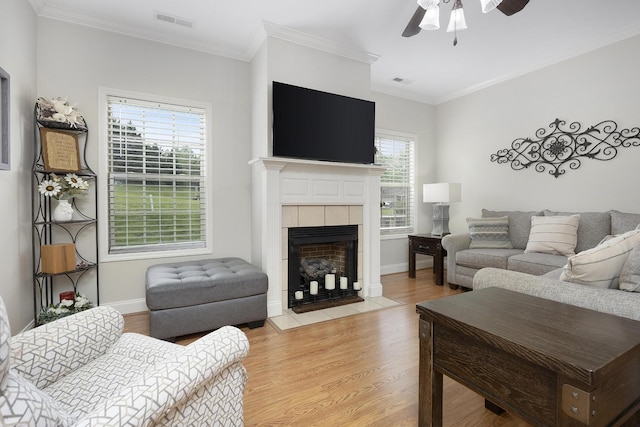 living area featuring a tiled fireplace, light wood-style floors, a ceiling fan, and visible vents