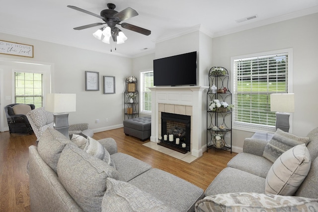 living room featuring visible vents, crown molding, wood finished floors, ceiling fan, and a tiled fireplace