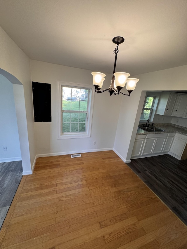unfurnished dining area with a sink, arched walkways, baseboards, wood finished floors, and visible vents