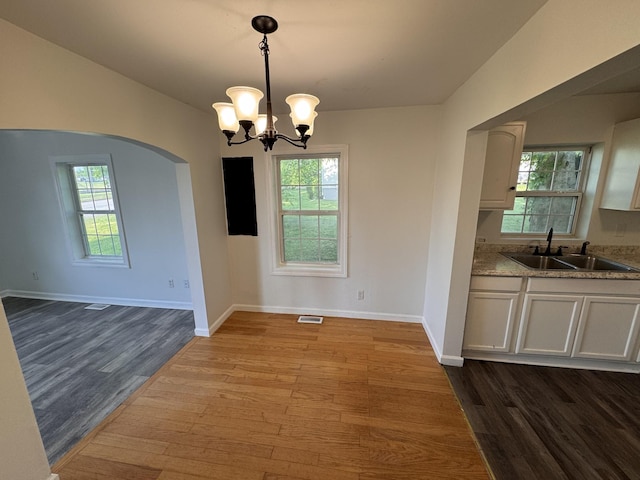 unfurnished dining area featuring visible vents, dark wood-style flooring, baseboards, arched walkways, and a sink