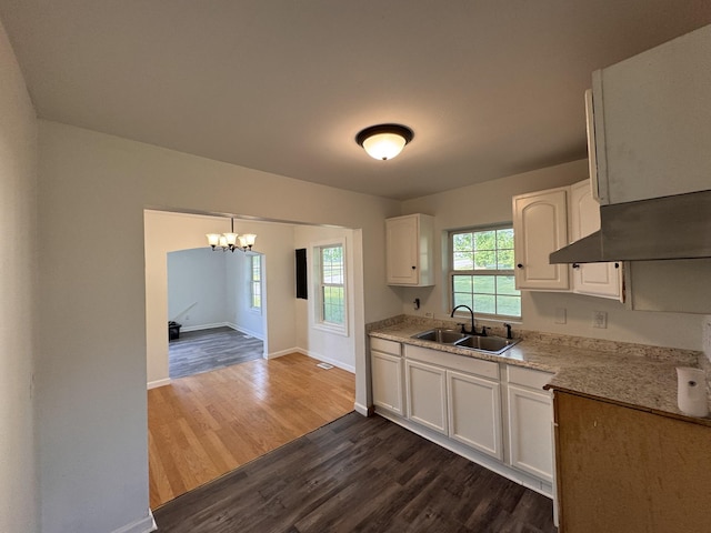 kitchen with white cabinets, a sink, a chandelier, baseboards, and dark wood-style floors