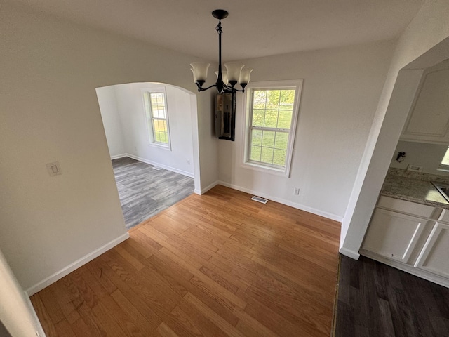 unfurnished dining area with baseboards, arched walkways, wood finished floors, and a chandelier