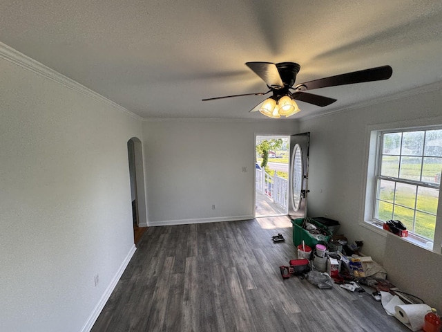 unfurnished room featuring ceiling fan, arched walkways, dark wood finished floors, baseboards, and ornamental molding