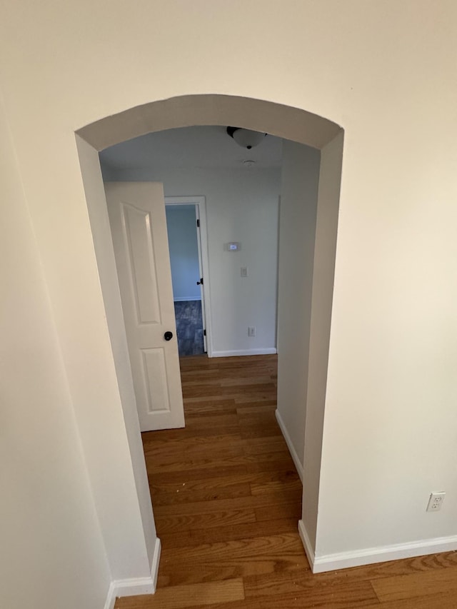 hallway featuring arched walkways, baseboards, and wood finished floors