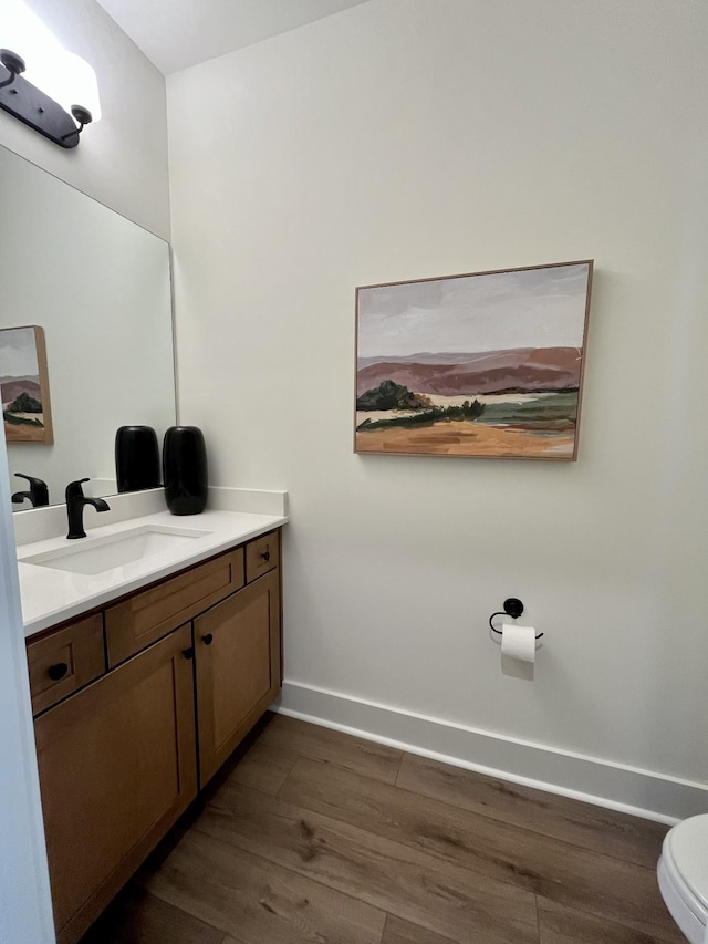bathroom featuring toilet, baseboards, wood finished floors, and vanity