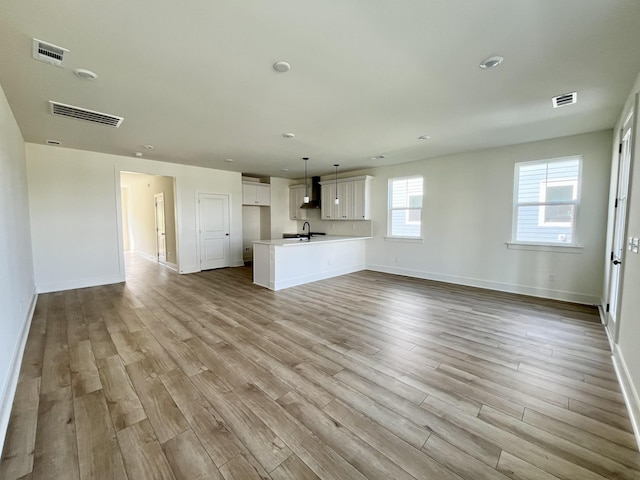 unfurnished living room with a sink, baseboards, visible vents, and wood finished floors