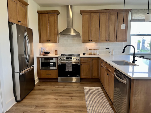 kitchen featuring wall chimney range hood, tasteful backsplash, wood finished floors, a sink, and stainless steel appliances