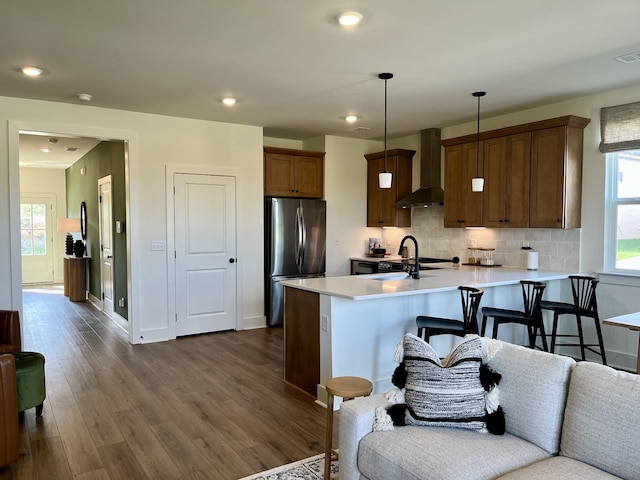 kitchen featuring freestanding refrigerator, a peninsula, wall chimney exhaust hood, and light countertops