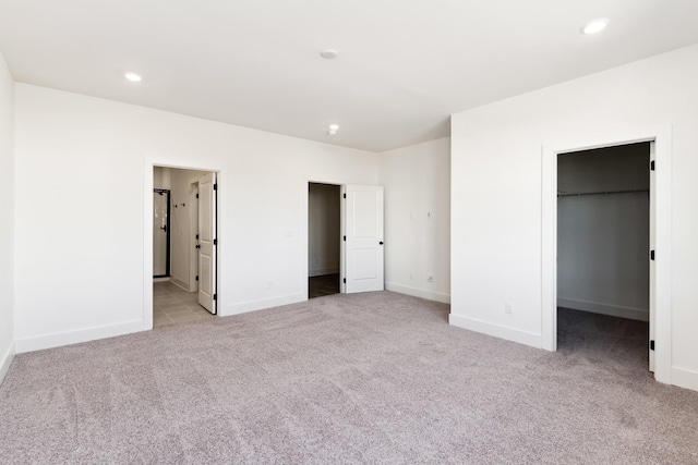 unfurnished bedroom with light colored carpet, recessed lighting, baseboards, and a spacious closet
