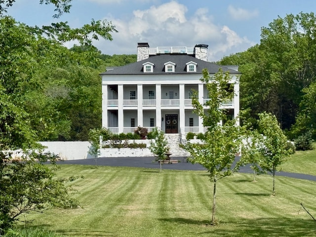 exterior space with a lawn, a balcony, a chimney, and a porch