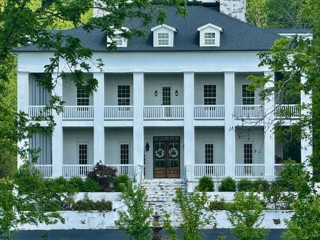 view of front of home featuring covered porch, french doors, a balcony, and a chimney