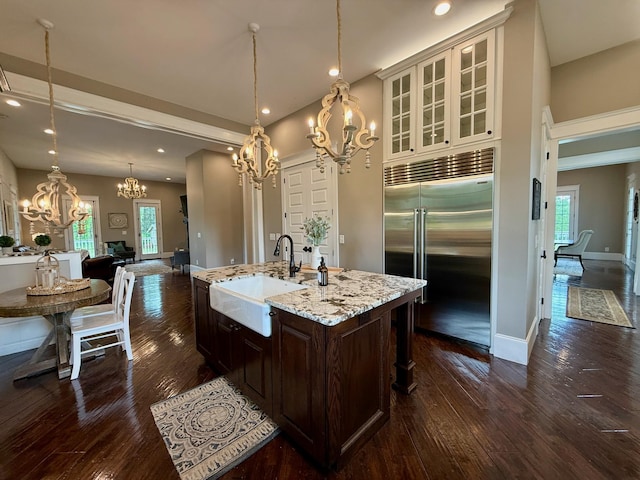 kitchen with an inviting chandelier, dark brown cabinetry, dark wood-type flooring, a sink, and stainless steel built in refrigerator