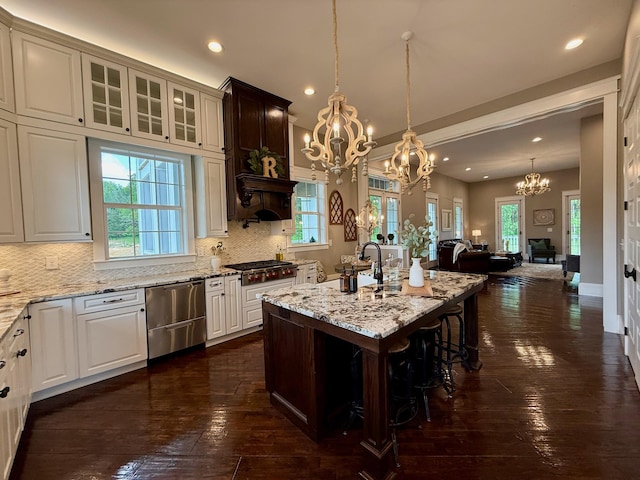 kitchen with dark wood-style flooring, light stone countertops, appliances with stainless steel finishes, a notable chandelier, and decorative backsplash