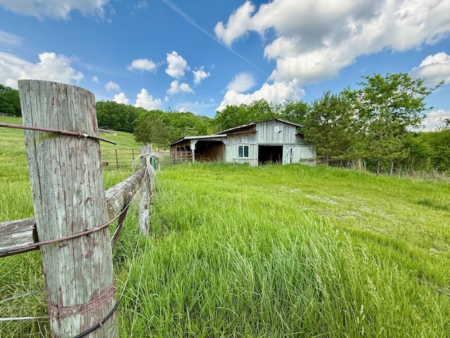 view of yard featuring a barn, a rural view, fence, and an outdoor structure