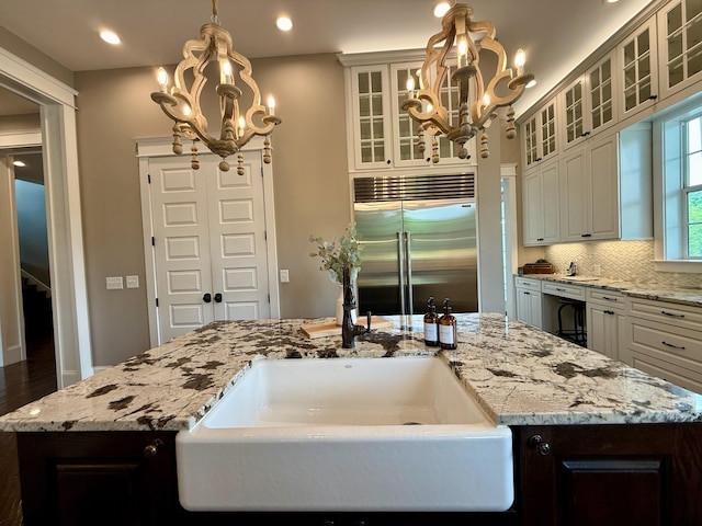 kitchen featuring stainless steel built in fridge, hanging light fixtures, a sink, a notable chandelier, and an island with sink