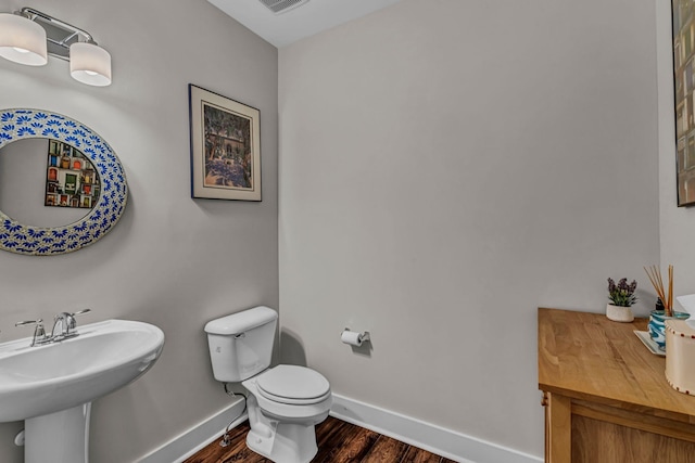 half bath featuring visible vents, wood finished floors, toilet, baseboards, and a sink