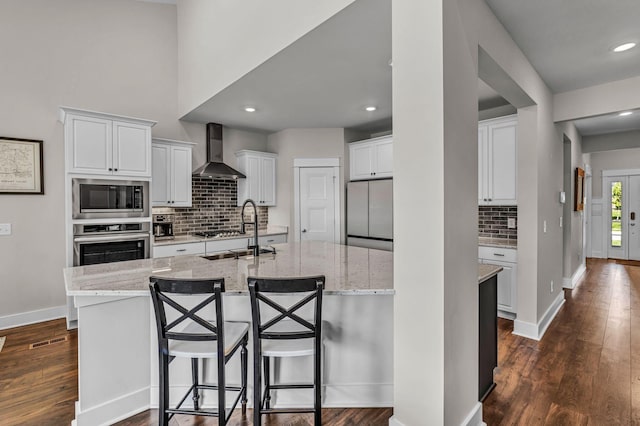kitchen with appliances with stainless steel finishes, a sink, wall chimney exhaust hood, tasteful backsplash, and a center island with sink