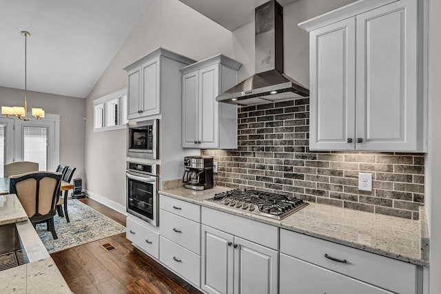 kitchen with wall chimney range hood, appliances with stainless steel finishes, an inviting chandelier, lofted ceiling, and tasteful backsplash