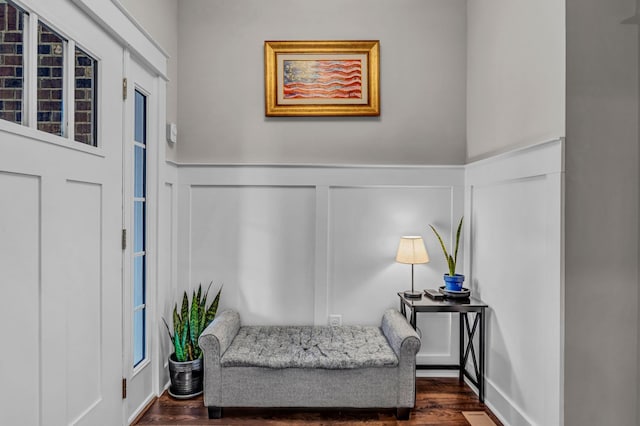 living area with dark wood-style flooring, a decorative wall, and wainscoting