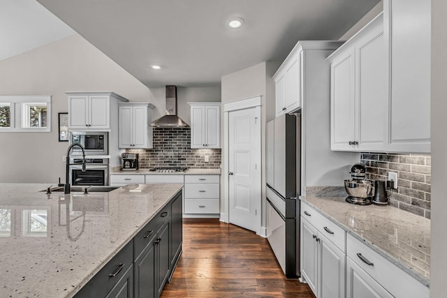 kitchen featuring wall chimney range hood, stainless steel appliances, white cabinets, and decorative backsplash