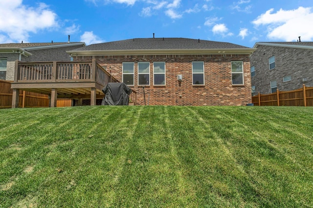 back of house with a lawn, fence, a wooden deck, and brick siding