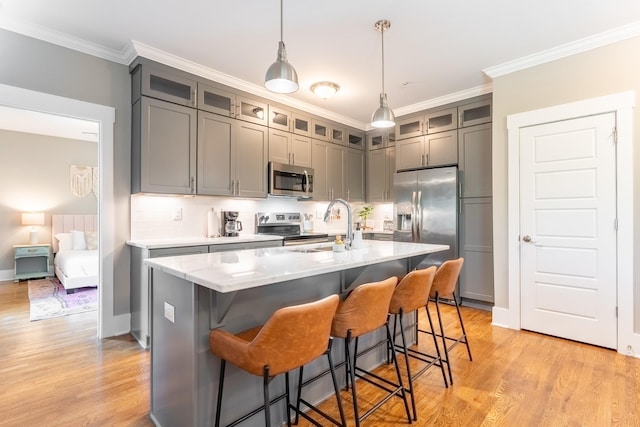 kitchen featuring appliances with stainless steel finishes, a sink, light wood-style flooring, gray cabinetry, and ornamental molding