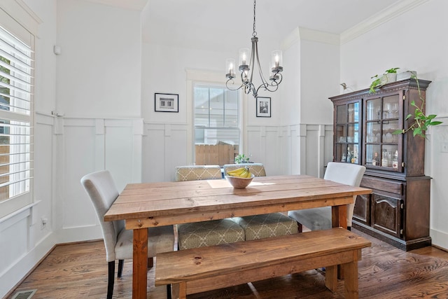 dining space featuring an inviting chandelier, wainscoting, wood finished floors, and a decorative wall