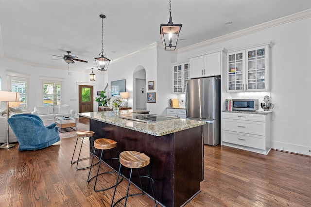 kitchen featuring a ceiling fan, appliances with stainless steel finishes, a center island, arched walkways, and dark wood-type flooring