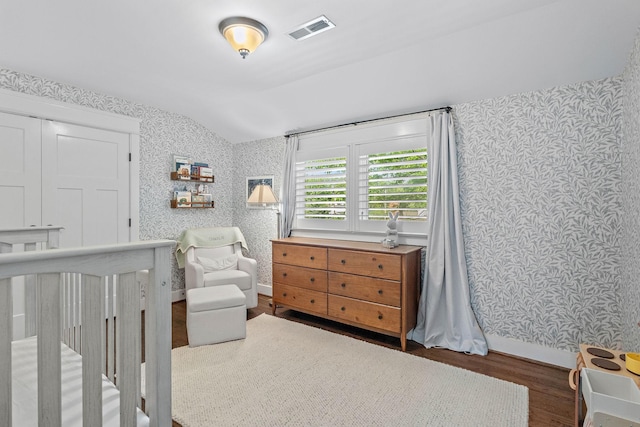bedroom with visible vents, lofted ceiling, wood finished floors, and wallpapered walls