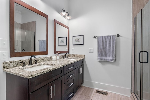 bathroom featuring a sink, a stall shower, double vanity, and visible vents