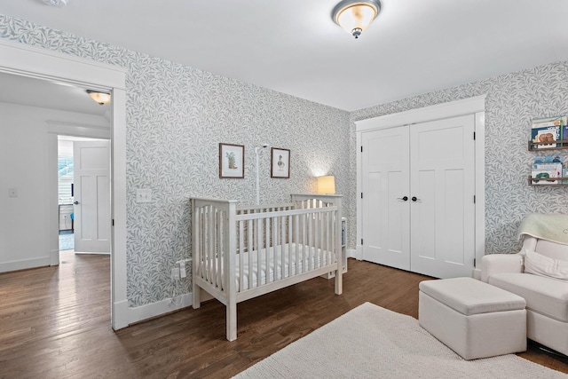 bedroom featuring baseboards, wallpapered walls, wood finished floors, and a closet
