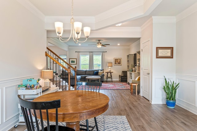 dining room with ornamental molding, wood finished floors, stairway, and ceiling fan with notable chandelier