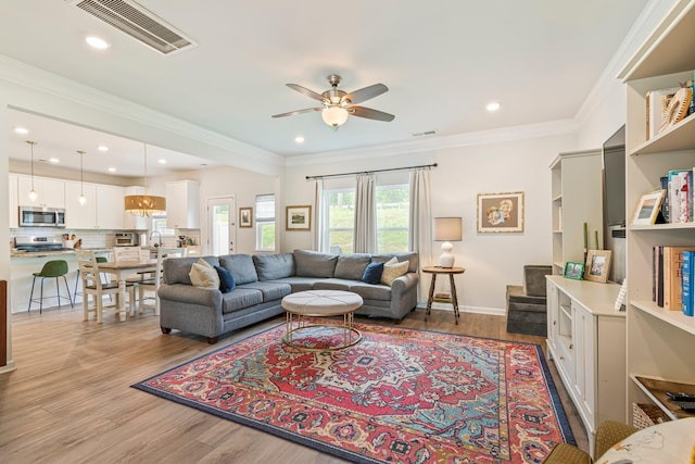 living area featuring light wood-style floors, ceiling fan, ornamental molding, and visible vents