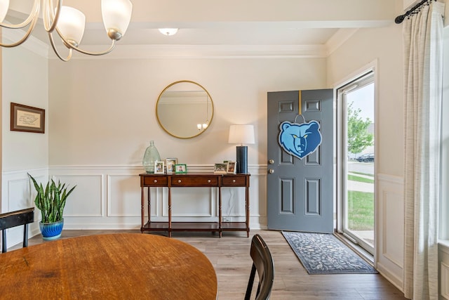 foyer with an inviting chandelier, ornamental molding, a decorative wall, and wood finished floors