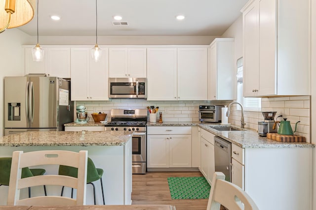 kitchen featuring a sink, light wood-style flooring, stainless steel appliances, a kitchen bar, and visible vents