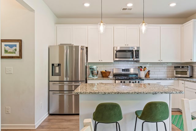 kitchen with visible vents, appliances with stainless steel finishes, a center island, white cabinets, and light wood-style flooring